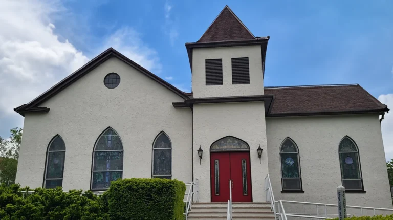 Freshly painted white stucco church exterior with arched windows and red entry doors