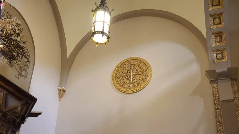 Gold decorative medallion on arched wall inside house of worship with hanging lantern