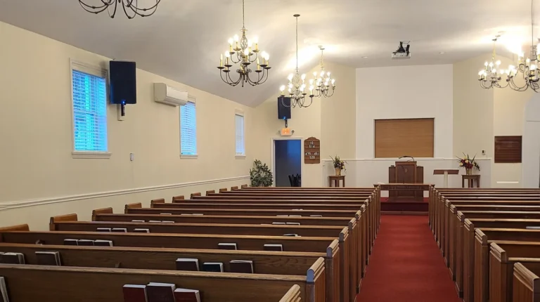 Freshly painted church sanctuary interior with rows of wood pews and chandeliers