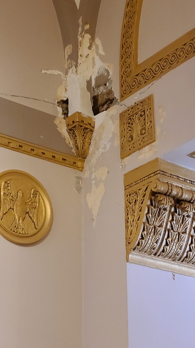 Collapsed and peeling ceiling plaster above ornate gold molding in a church interior