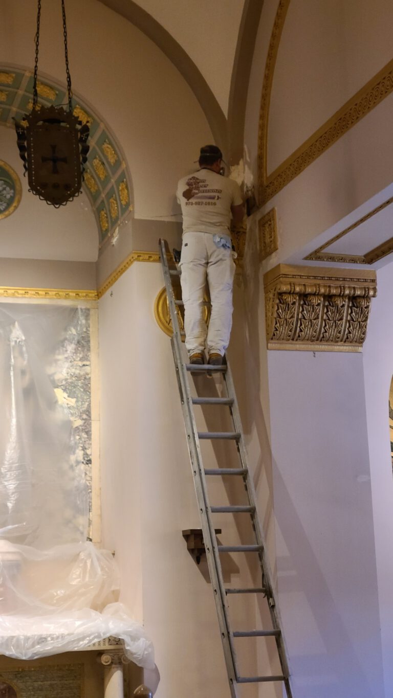 Worker on ladder painting upper wall of ornate house of worship interior