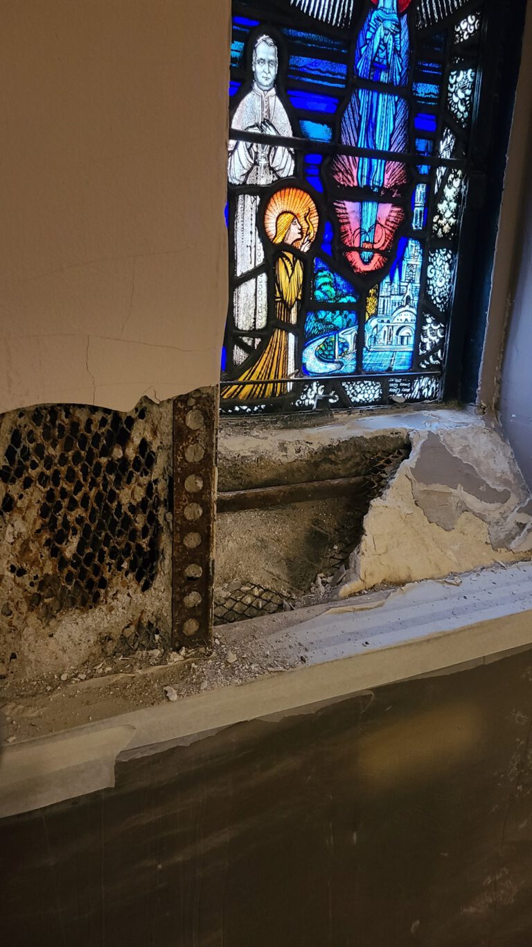 Crumbling stone sill and exposed substrate beneath stained glass window in church interior