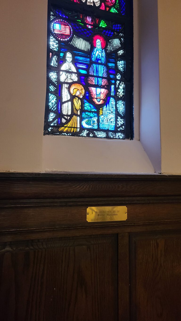 Colorful stained glass church window above wood paneling with small brass plaque